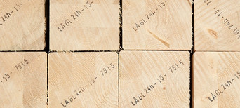 Gestapelte Brettschichtholzbalken mit sichtbarer Jahresringstruktur und Markierungen für den Holzbau.